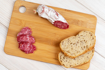 Sliced cereal bread and slices of dried Italian flask on a wooden cutting board. Simple food for a snack at home
