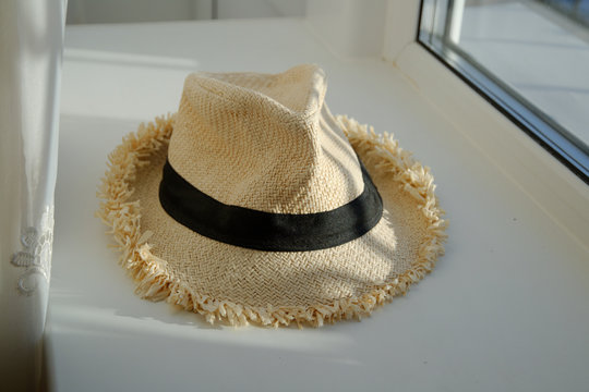a white summer hat with a black ribbon lies on a white windowsill.