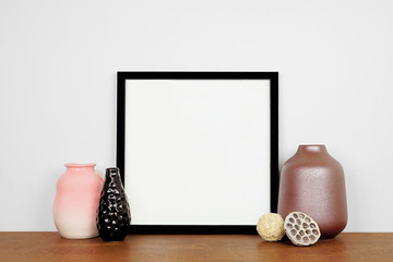 Mock up black square frame with vase home decor. Wooden shelf against a white wall. Copy space.