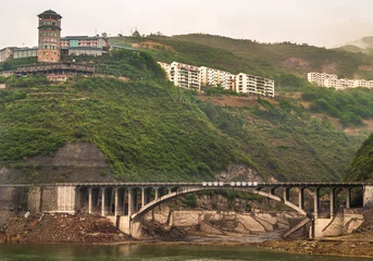 Foto op Canvas Baidicheng, China - May 7, 2010: Qutang Gorge on Yangtze River. Brown concrete road bridge along shore over sanded inham set in a green mountain landscape with multi-level residential housing on top. © Klodien