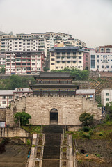 Fototapeta na wymiar Baidicheng, China - May 7, 2010: Qutang Gorge on Yangtze River. Portrait of historic town Gate and highrise housing under White mist over hills. Long steep stairway leads up.