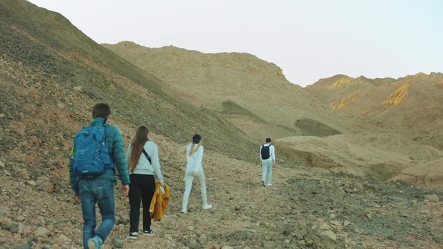 Group of tourist walk along the rock canyon in hot desert, tourists take picture and have fun. Desert mountains background, Egypt, Sinai, slow motion, full hd