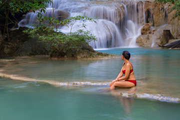 Fototapeta premium Woman in red bikini look water at Erawan Waterfall and natural