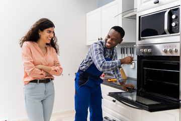 Woman Looking At Worker Repairing Oven