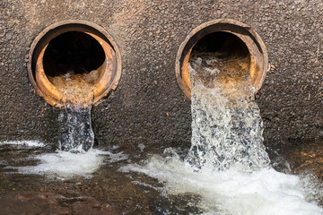 Water flowing from pipes under causeway on road
