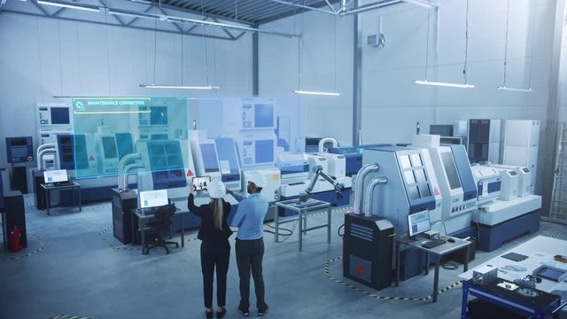 Industry 4.0 Factory: Two Engineers Uses Digital Tablet Computer with AR Software to Connect with High-Tech CNC Machinery, Robot Arm and Visualize Maintenance and Diagnostics of the Equipment