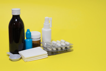 Tissues, nose drops, cough syrup, spray, pills and blister on yellow background. Cure illness and epidemy concept