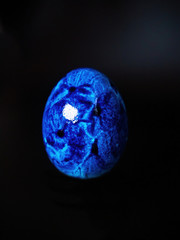 vertical photo of a blue colored egg on a sad black background