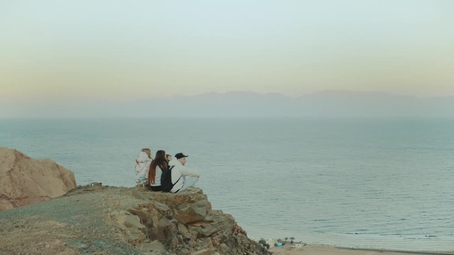 Group of friends relaxing on top of a mountain on sunset and enjoying sea view - friendship, youth, slow motion, full hd