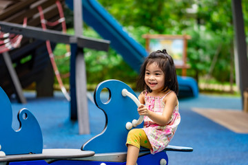 Fototapeta na wymiar Pretty asian little girl while sitting and playing on a see saw in a playground