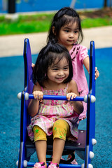 Fototapeta na wymiar Pretty asian little twins girls while sitting and playing on a see saw in a playground