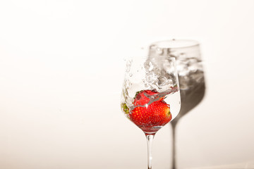 A strawberry falling into a glass of water, creating splashes. Isolated on white background, with a shadow. 
