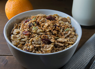 Cereal and granola in a white bowl, with a glass with milk and orange on the side, on a rustic wooden table as part of a breakfast