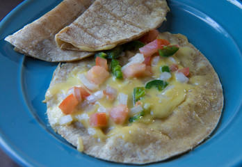 Quesadilla with pico de gallo or salsa bandera on a blue plate, a traditional Mexican snack.