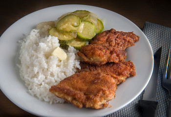 Boneless breaded chicken legs with steam rice and vegetables on the side.