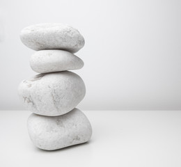Fototapeta na wymiar Tall stack of white stones or pebbles on white table with white wall background