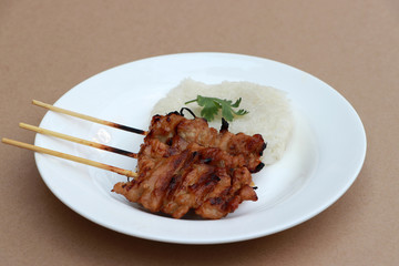 Three Grilled pork skewers with glutinous rice on the white plate on brown floor.
