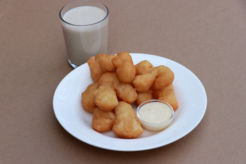 Chinese doughnut stick with Sweetened condensed milk in the small glass cup on the white round dish with a glass of milk on brown floor.