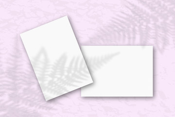 2 sheets of white textured paper against a pink wall. Mockup with an overlay of plant shadows. Natural light casts shadows from the fern leaves. Flat lay, top view