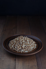 Boiled buckwheat porridge in a clay plate on a wooden background. Copy space. Dishes menu.