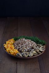 Buckwheat porridge with carrots and onions, mushrooms and dill. Traditional Russian lenten dish. Vegetarian menu. Rustic wooden background with place for text. Copy space. Ready to eat. Homemade food.