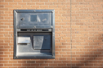A night and day deposit box drop off on the light brown brick wall - Powered by Adobe