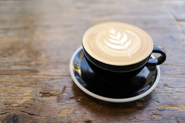 Latte art on cafe latte in a black cup on a wooden table