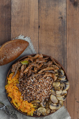 Buckwheat porridge with pieces of beef meat, mushrooms and carrot. Top view of food plate on wooden background with copy space. 