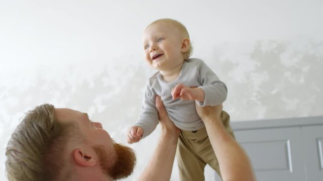 Handheld shot of happy bearded father lifting and kissing giggling baby girl