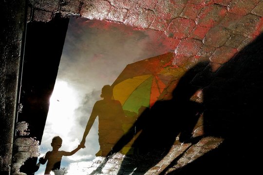 Reflection Of Child With Parent On Puddle