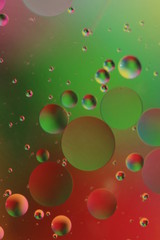 Obraz na płótnie Canvas macro of oil mixed with water on colorful red, pink, green and orange background, colourful circles, copy space, vertical