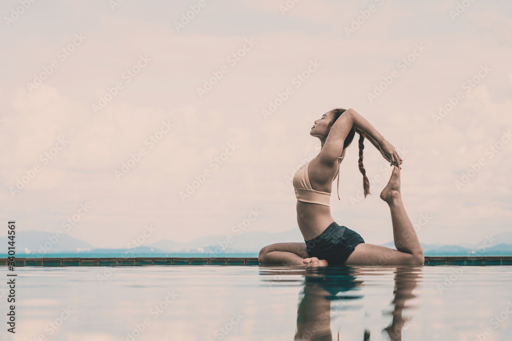 Wall mural vacation of attractive asian woman relaxing in yoga king pigeon pose on the pool above the beach wit