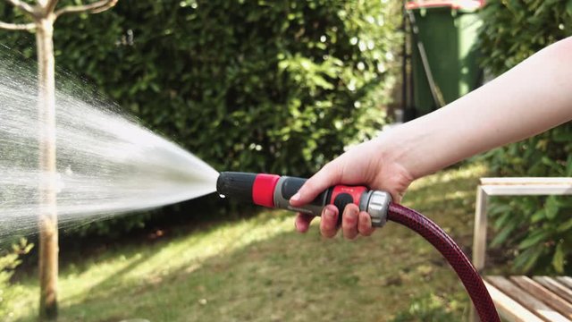 Hand gie&szlig;t mit Gartenschlauch Blumen oder Beet, unscharfer Hintergund, Bew&auml;sserung im Garten