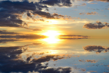 Fototapeta na wymiar Sunrise or sunset in Uyuni salt flat (Bolivia) the biggest salar in the world covered with water and reflecting like a mirror the sky, the clouds and the sun in an orange, blue, white and yellow image