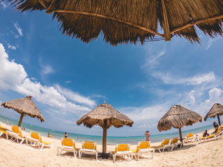 Straw beach umbrellas, white and yellow beach chairs, and the caribbean beach on a sunny day, Playa Paraíso, Mexico