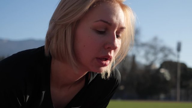 Girl athlete straightens her hair before a run in an open stadium on a clear summer day. Inhales and exhales deeply. And makes a breakthrough at the start.