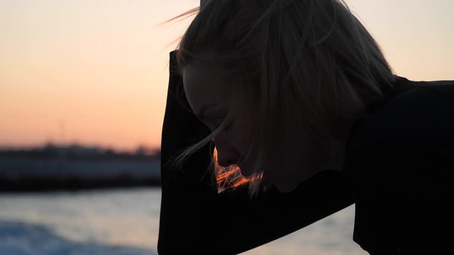 The girl regains her breath after an evening run along the embankment of the sea pier against the backdrop of sunset and sea breeze. Healthy lifestyle. Keeping fit.