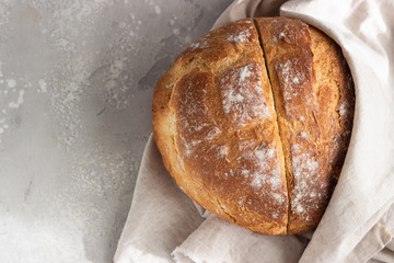 Round loaf of freshly backed artisan sourdough bread. No knead bread. Top view, copy space. Light grey concrete background.