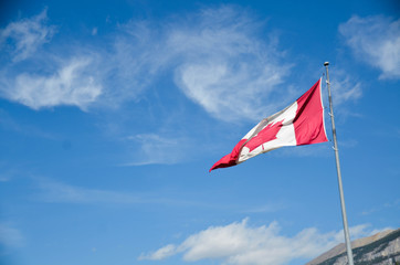 pov to a flag of canada with background of blue sky with some cloud in summer daytime