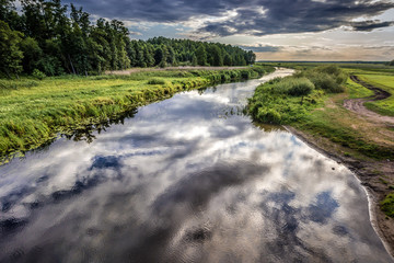 Clouds reflecting in the Biebrza River, view from a bridge in Dolistowo village, Poland