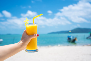 First-person view. Girl holds a glass cup of cold mango fresh on the background of a sandy tropical beach. White sand and a boat. Fairytale vacation in Thailand