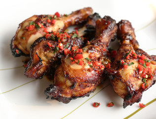 Baked chicken drumsticks. Served on white plate with minced chilly and mint leaves.