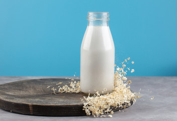 Dairy free,vegan Oat milk in a bottle with oat flakes on wooden cutting board.