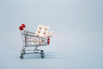 Shopping cart with pills, thermometer, syringe and money. The concept of medicine, insurance, shopping and expenses.