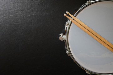 Drum stick and drum on black table background, top view, music concept