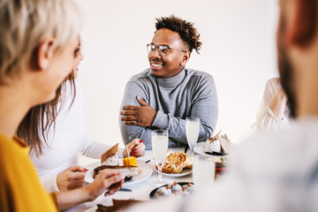 Attractive african american man sitting at dinning table with friends for lunch, smiling and chatting.