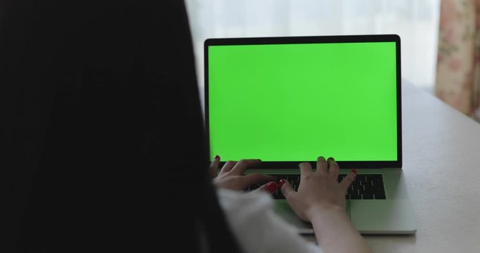 Female person typing on laptop keyboard with green screen on table