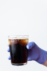 human hand with protective glove holding a glass of cola. Concept for celebrating the end of the coronavirus crisis, covid 19