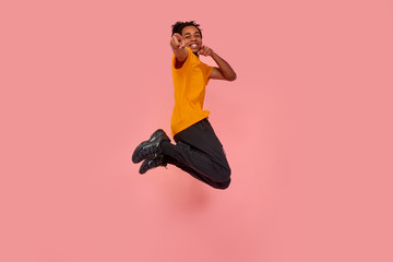 Full length shot of young surprised dark skinned man jumping in the air and pointing, choosing something, isolated on pink studio background. Freedom of choices, inspiration, human emotions concept