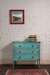 White brick wall with shabby chic vintage turquoise cabinet and hanged painting in living room,...